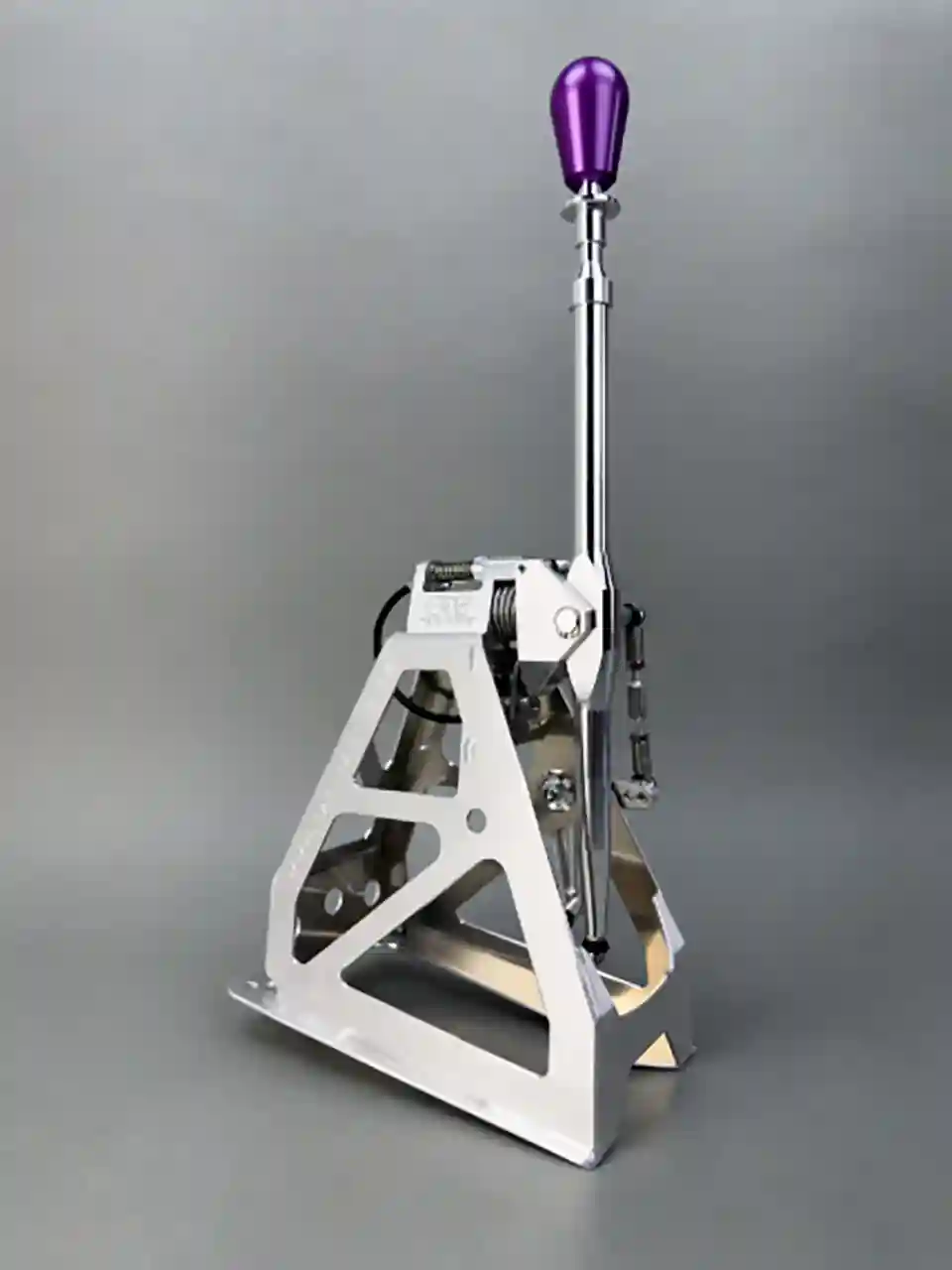 Studio shot of a CAE Ultra Shifter made of silver-colored aluminum with a purple shift knob for the Ford Fiesta (2001–2008) on a gray background.